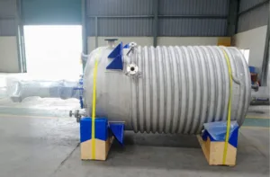 cylindrical high-pressure reactor in stainless steel with a limpet coil reactor is resting on a wooden pallet
